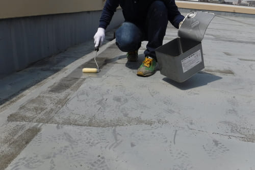 屋上防水工事中の写真 職人がローラーを使って塗装している様子