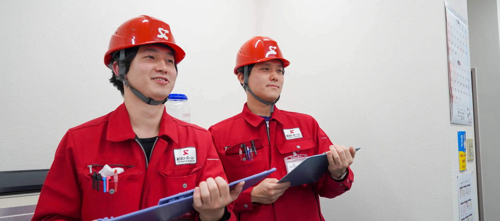 新日本コーポレーションの赤い作業着・ヘルメットを被った男性2人がバインダーをもって調査している写真